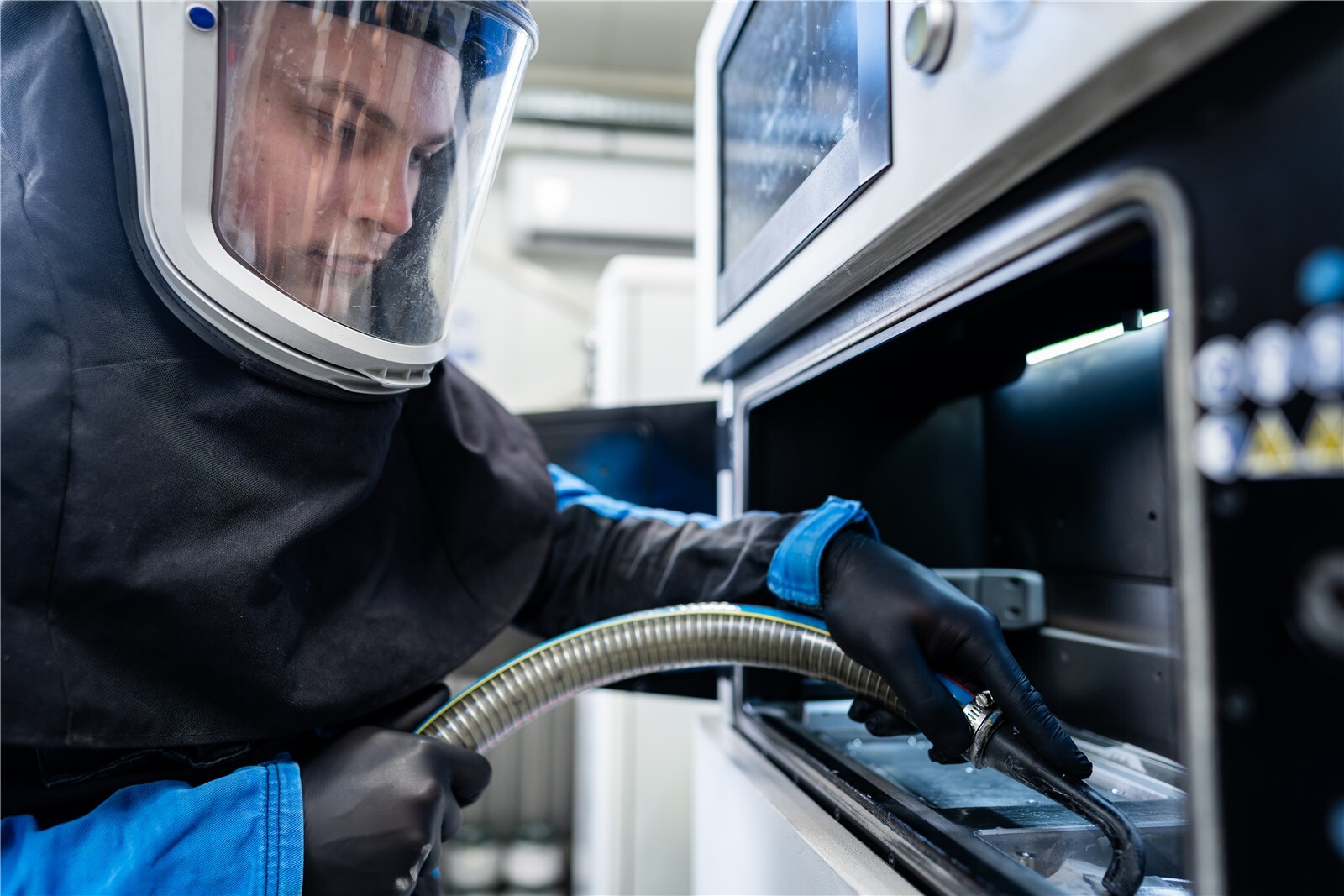 Mitarbeiter in Schutzausrüstung entfernt Restpulver aus dem Metall-3D-Drucker